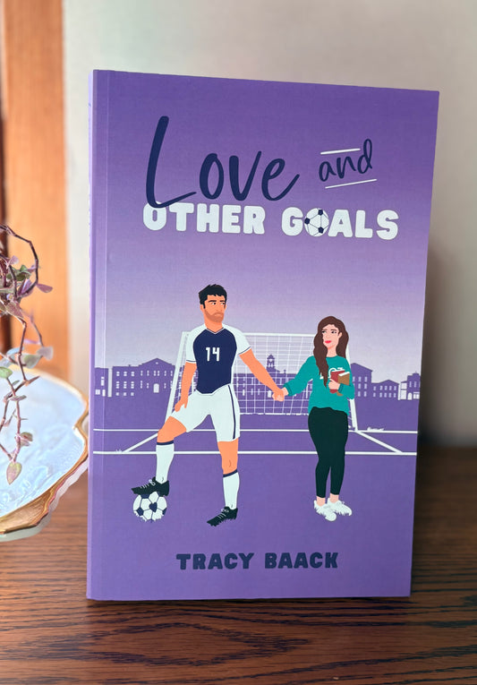 Book titled 'Love and Other Goals' by Tracy Baack on a wooden surface.