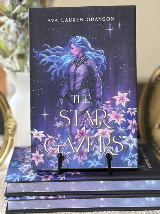 "Front cover of The Stargazers by Ava Lauren Grayson displayed in a book cradle on top of a stack of books."
