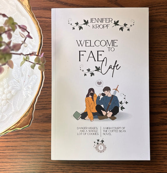 Book titled 'Welcome to Fae Cafe' by Jennifer Kropf on a wooden surface with decorative elements.