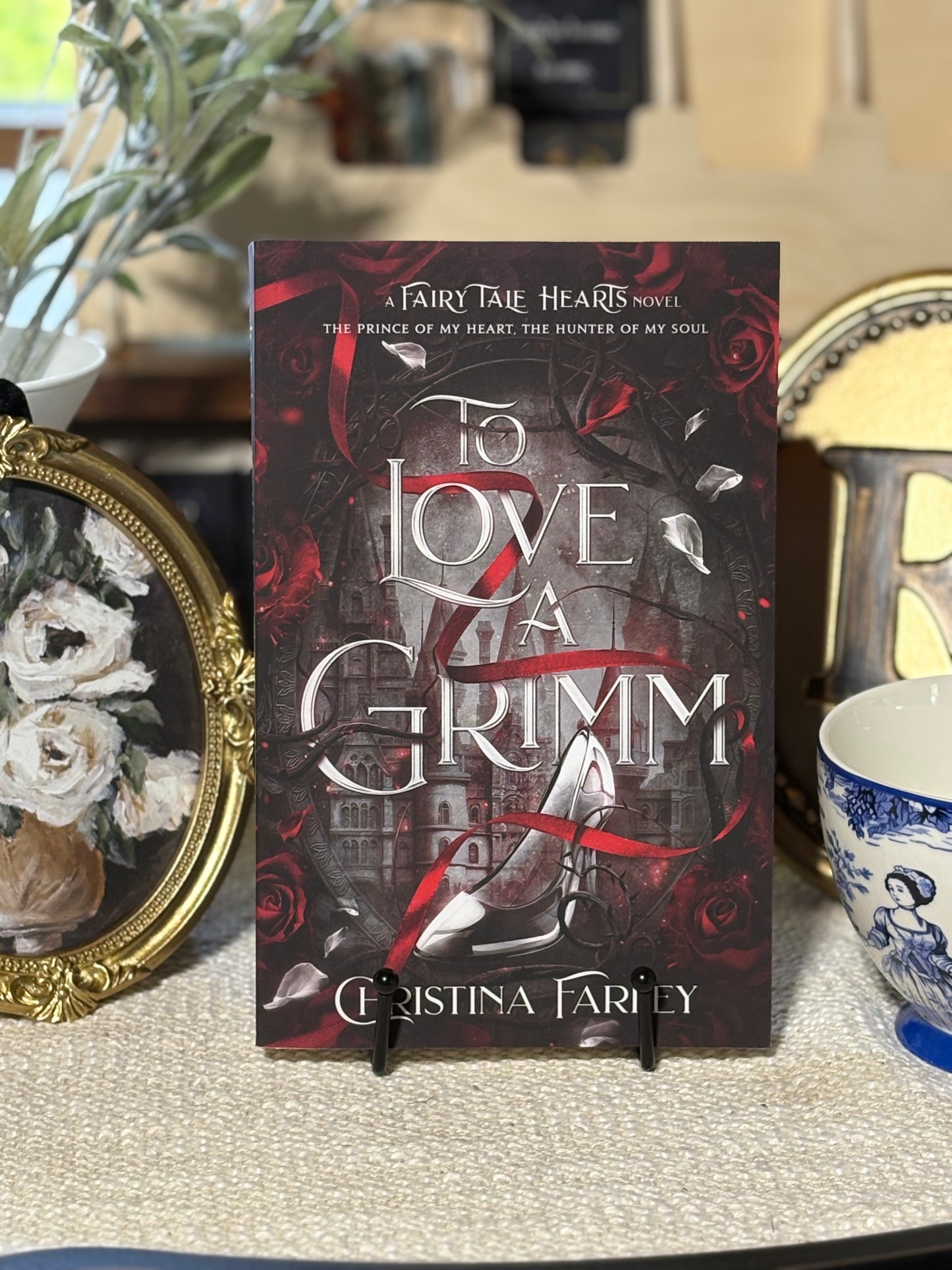 Book titled 'To Love a Grimm' by Christina Farley on a stand with decorative items in the background.